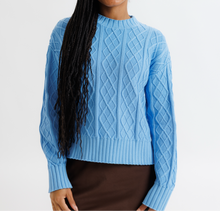 Woman wearing a blue cable knit sweater against a plain background