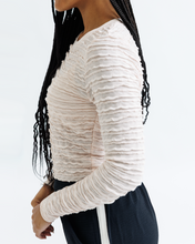 Person wearing a white textured long-sleeve top on a light gray background