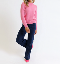Woman wearing a pink sweater and navy pants on a white background