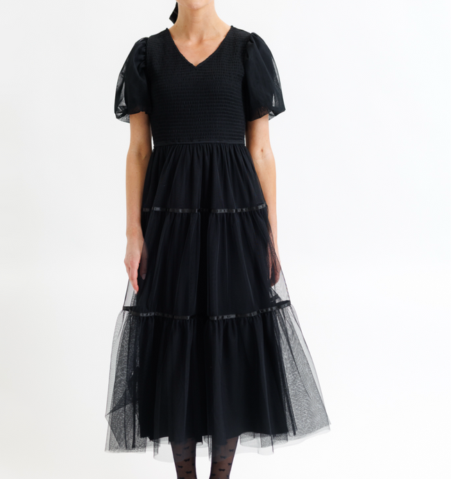Woman wearing a black dress with sheer sleeves and bottom tulle layer on a white background