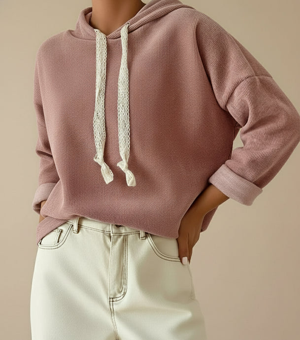 Woman wearing a dusty pink hoodie with white lace drawstrings and light-colored pants on a beige background