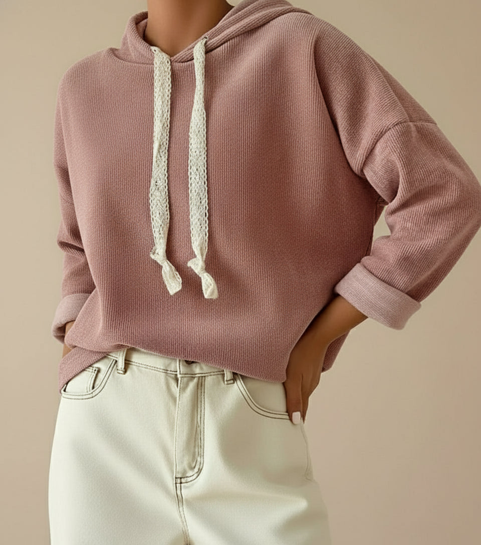 Woman wearing a dusty pink hoodie with white lace drawstrings and light-colored pants on a beige background